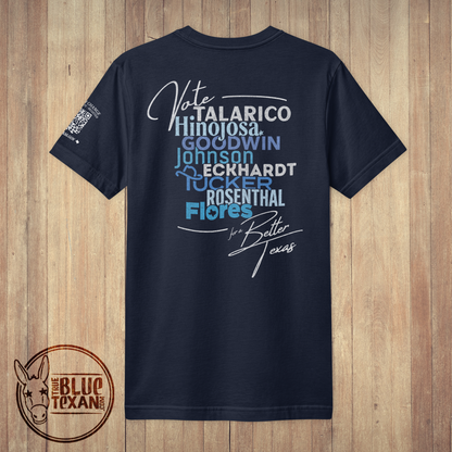 A navy blue short-sleeve t-shirt with a political graphic on the back, displayed flat against a light brown wood plank background. The graphic features text including 'Vote TALARICO Hinojosa', 'GOODWIN JOHNSON', 'ECKHARDT', 'ROSENTHAL', and 'Flores' in white and light blue, along with a signature and 'for Better Texas'.