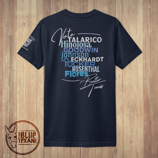 A navy blue short-sleeve t-shirt with a political graphic on the back, displayed flat against a light brown wood plank background. The graphic features text including 'Vote TALARICO Hinojosa', 'GOODWIN JOHNSON', 'ECKHARDT', 'ROSENTHAL', and 'Flores' in white and light blue, along with a signature and 'for Better Texas'.